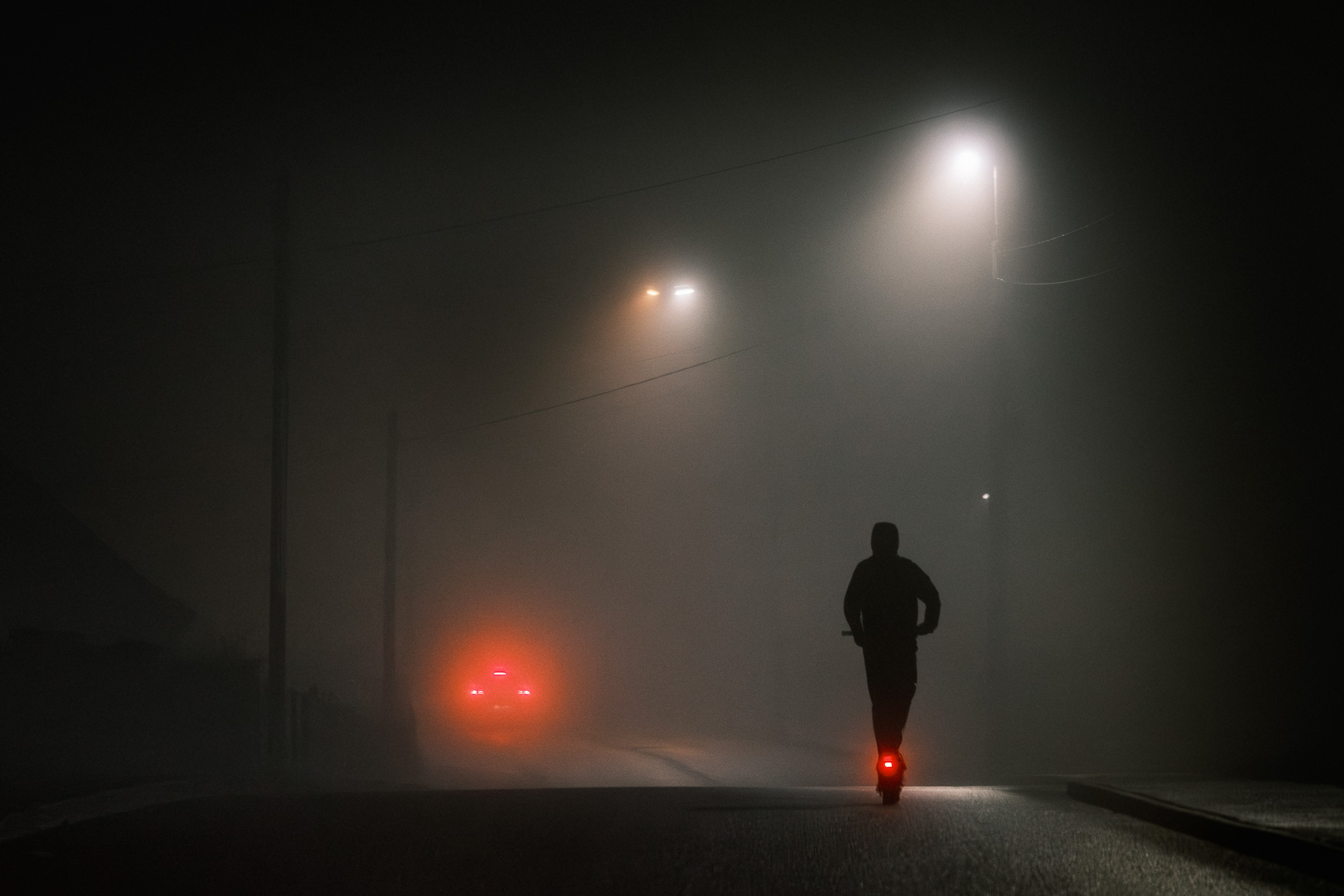Person riding an electric scooter through a foggy street in Cork at night, with car lights visible in the distance